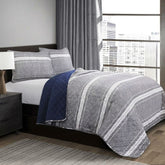 A bed featuring a gray and blue striped comforter, neatly arranged with pillows at the headboard.